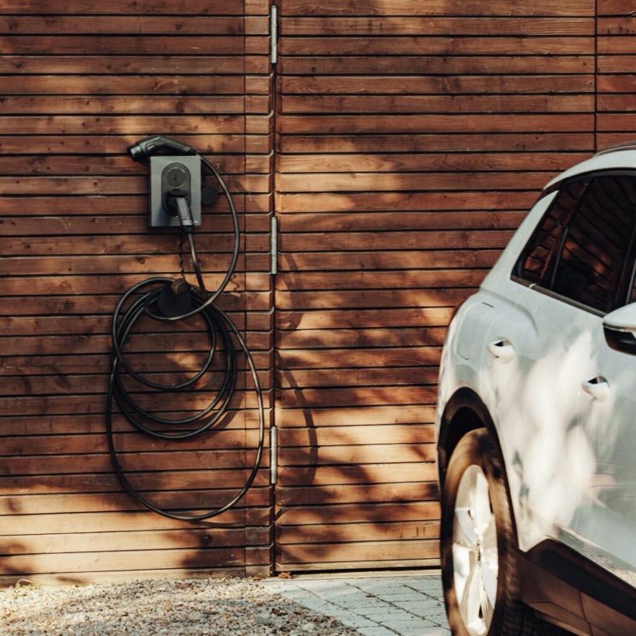 Omakotitalon seinään asennettu latausasema ja sähköauto